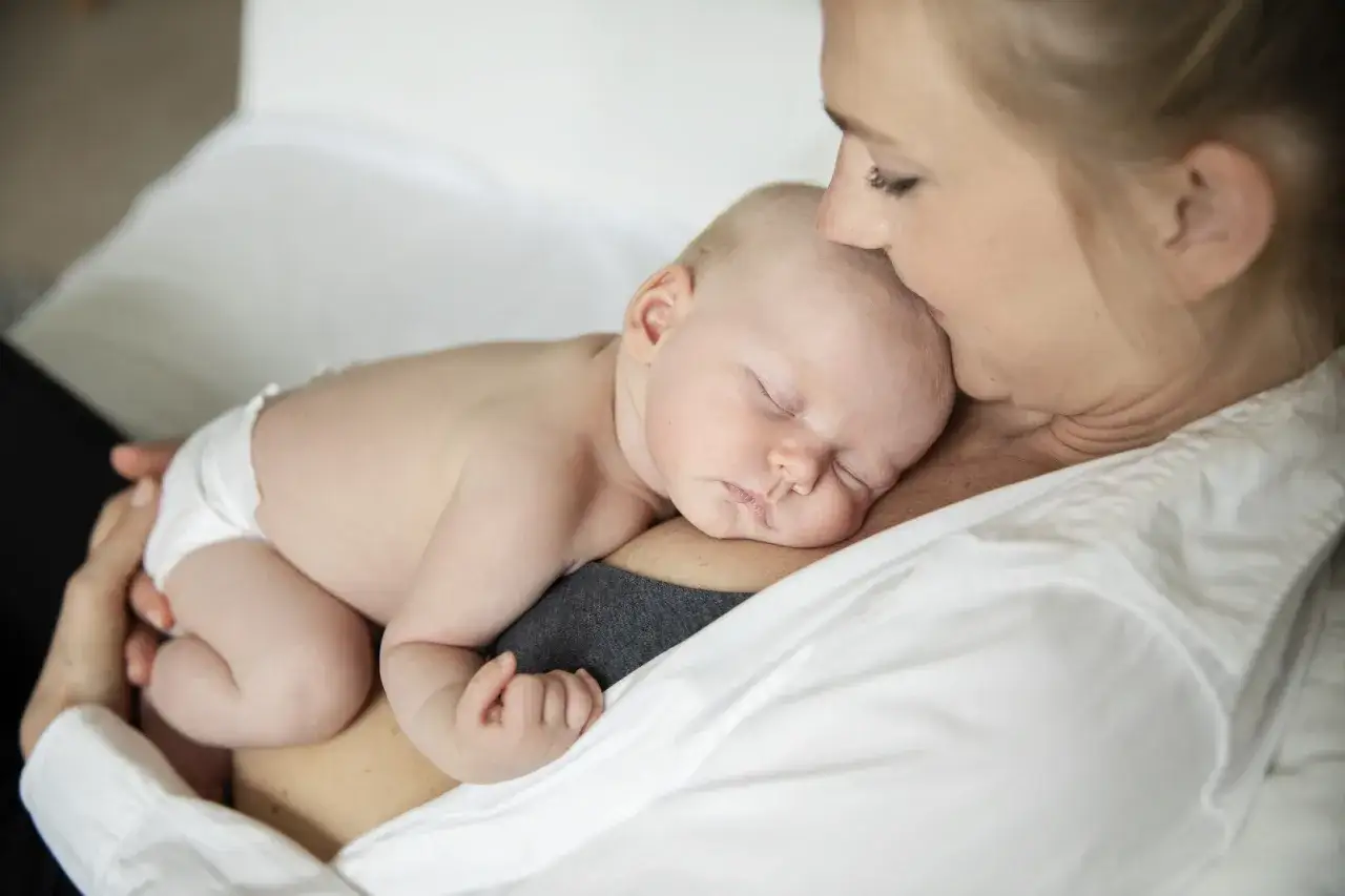 En mamma h&aring;ller sitt sovande sp&auml;dbarn mot br&ouml;stet. Bebisens mage &auml;r rund och mjuk, en perfekt bebis mage storlek.