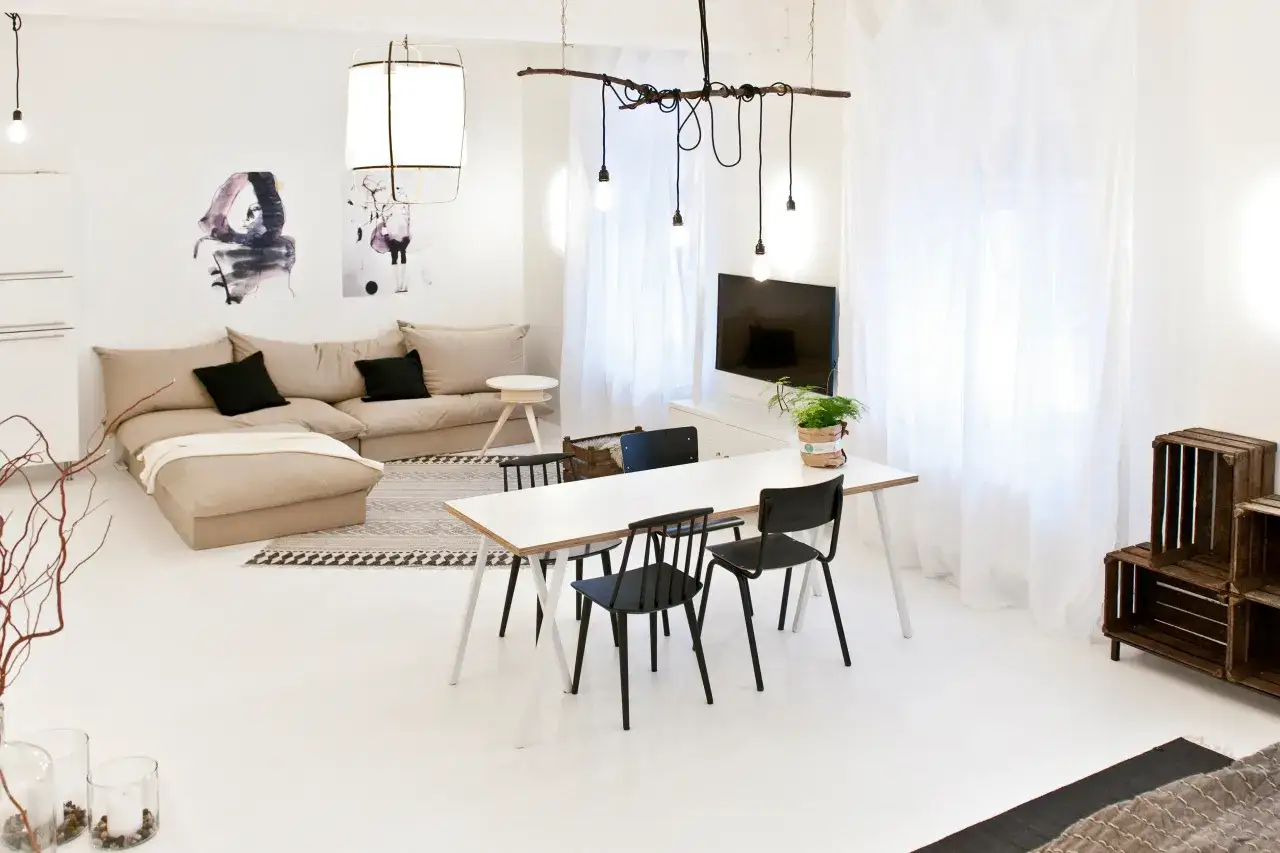 Helle, moderne Wohnung mit beigem Sofa, weißem Esstisch und schwarzen Stühlen. Weiße Vorhänge und Kunstwerke an der Wand machen die dunkle Wohnung heller.