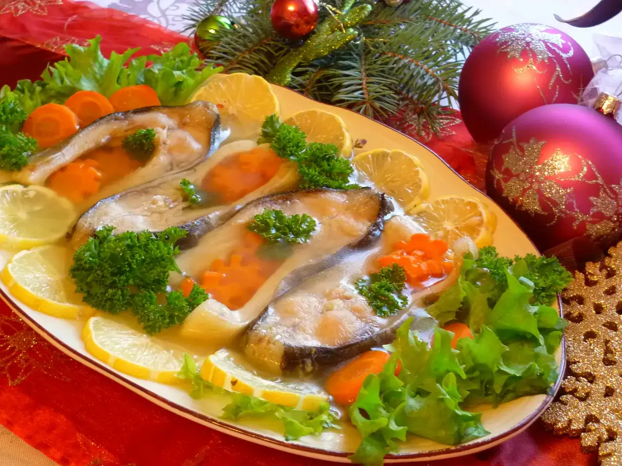 Elegancki filet z karpia w galarecie, ozdobiony marchewką, cytryną i natką pietruszki, na świątecznym stole.
