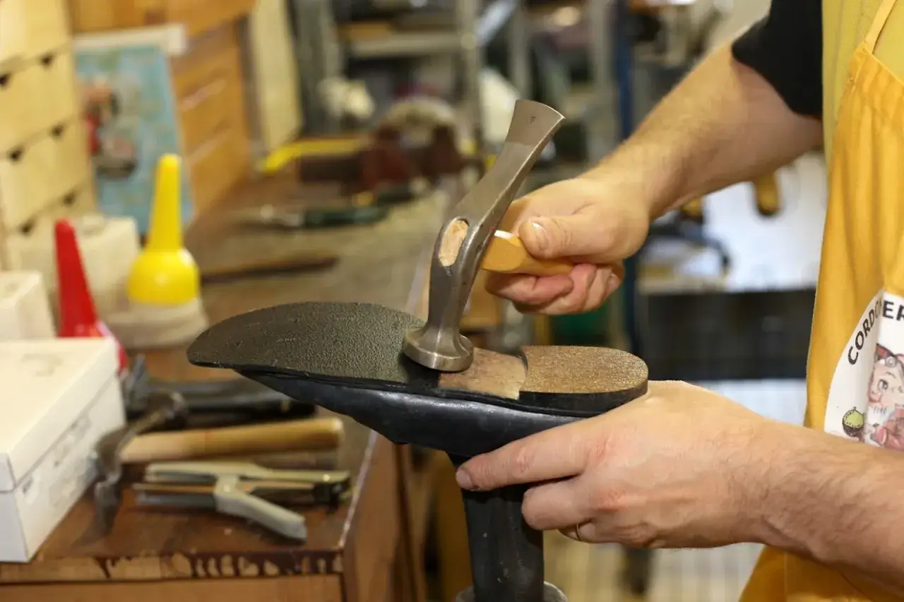 Un cordonnier r&eacute;pare des chaussures trou&eacute;es, martelant une nouvelle semelle sur une forme.