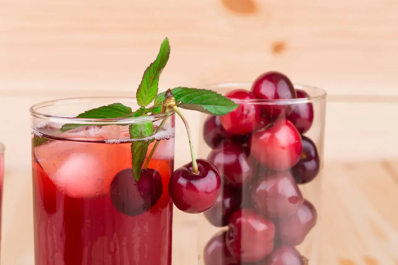 Erfrischender Sauerkirschsaft mit Eis und Minze, daneben ein Glas voller Kirschen. Die Wirkung von Sauerkirschsaft ist bekannt für seine entzündungshemmenden Eigenschaften.