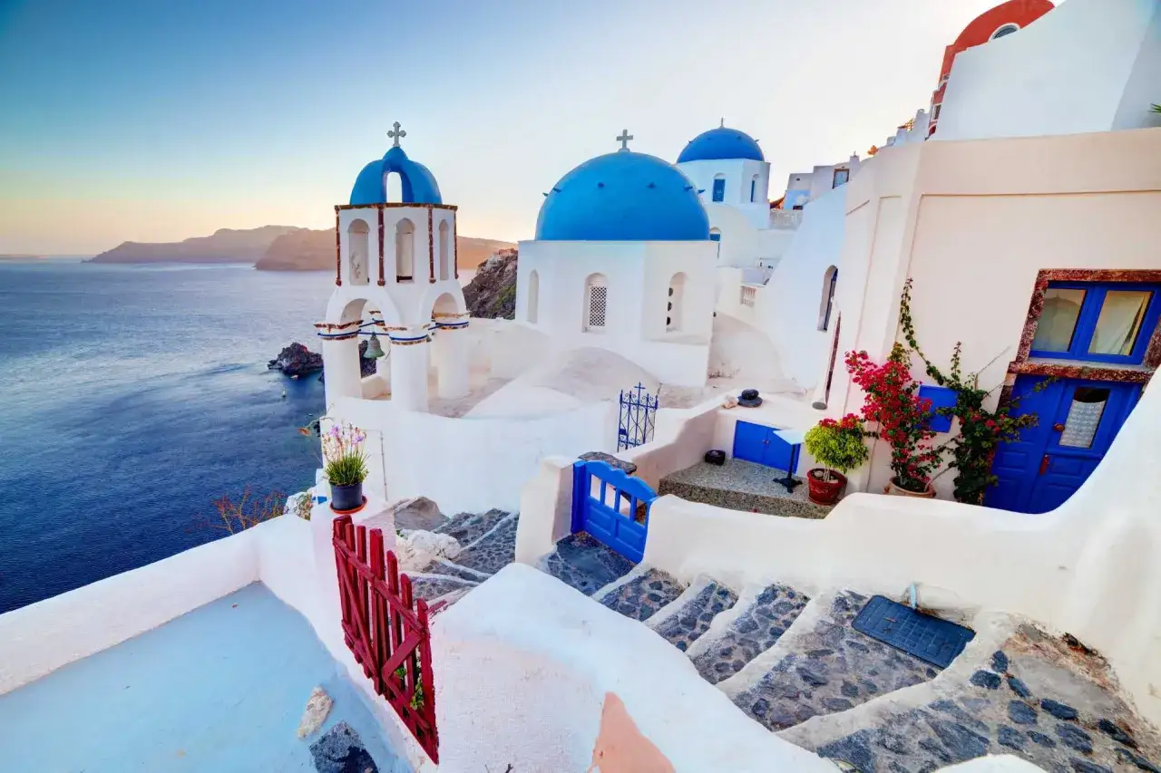 Białe domy z niebieskimi kopułami na Santorini, malownicze schody i widok na morze. Ceny wakacji na Santorini mogą być wysokie, ale widoki są bezcenne.