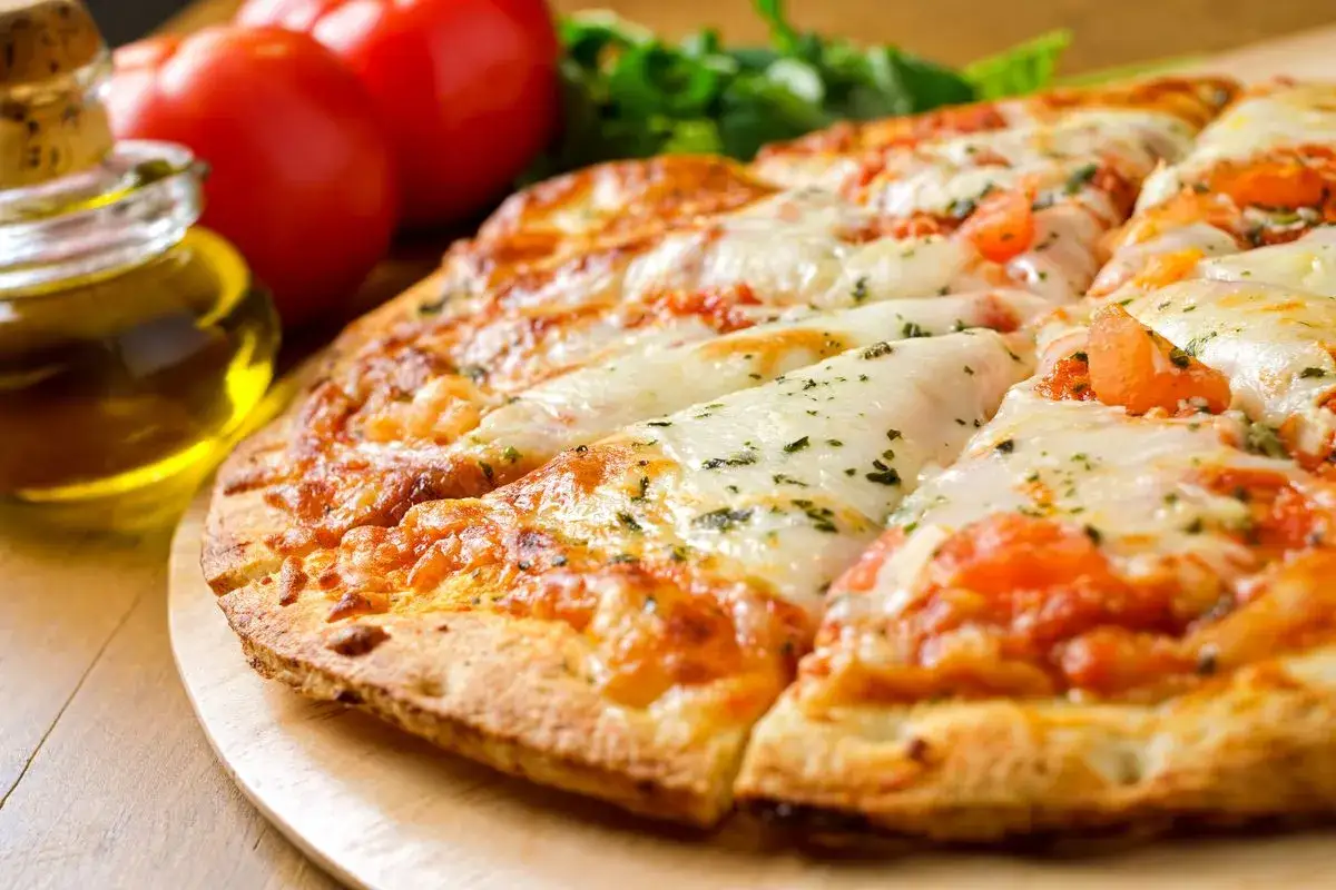 Pizza senza lievito dorata e filante, con pomodoro fresco, mozzarella e basilico. Accanto, pomodori rossi e un vasetto d'olio.