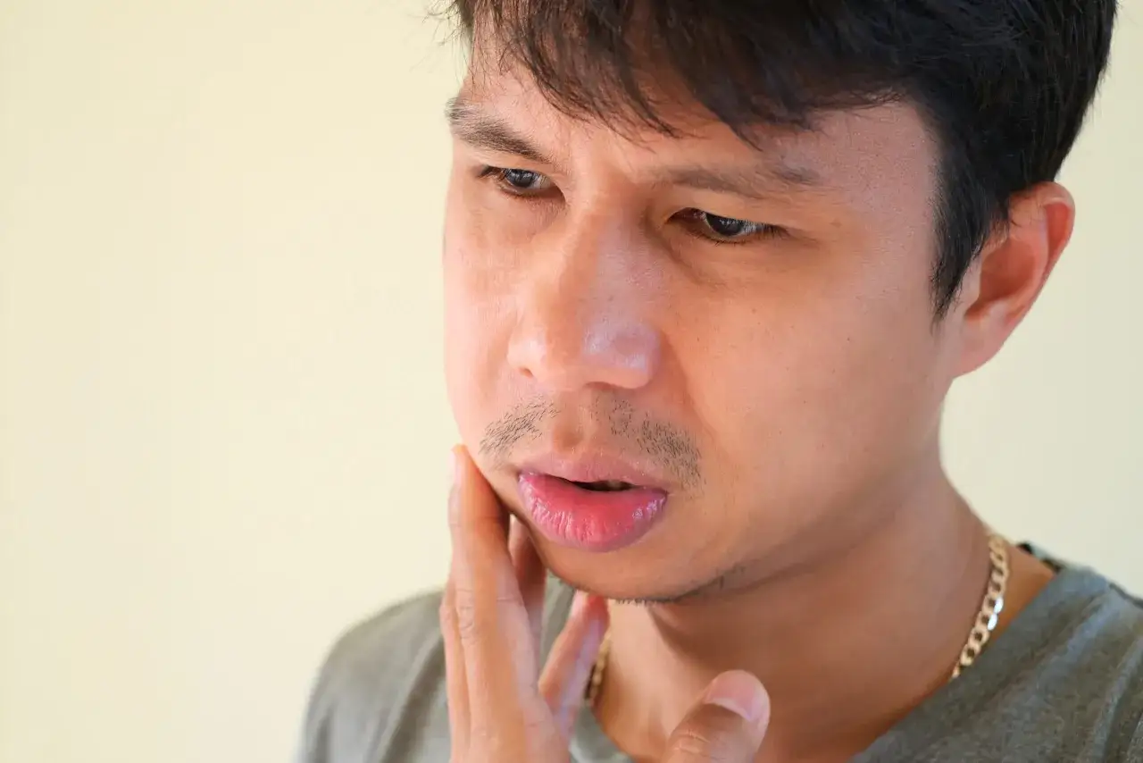 Uomo con mano sulla guancia, preoccupato per un dolore che potrebbe richiedere un antibiotico per denti e gengive.