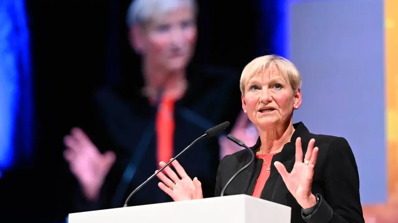Frau spricht bei der EKD Synode, im Hintergrund ein großes Bild von ihr mit roter Krawatte.