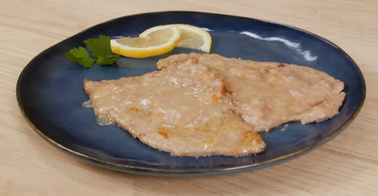 Due scaloppine al limone, succulente e dorate, servite su un piatto blu con spicchi di limone e prezzemolo.