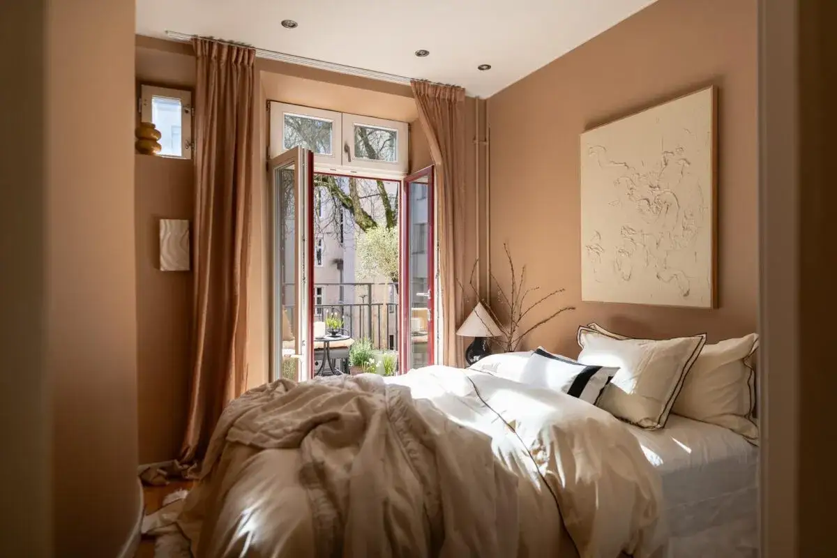 Acogedor dormitorio con paredes color terracota, cama vestida con funda nordica terracota y balc&oacute;n abierto.