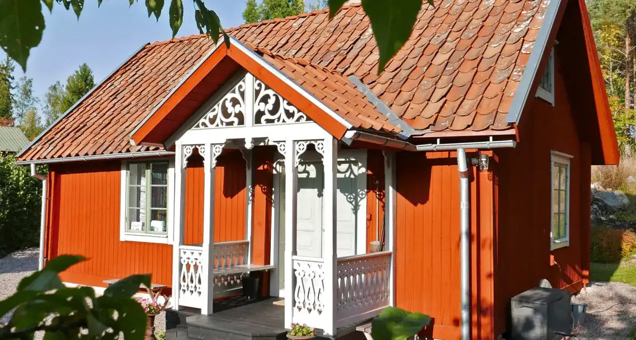 R&ouml;tt hus med vacker, vitm&aring;lad farstukvist. En b&auml;nk finns att sitta p&aring;.