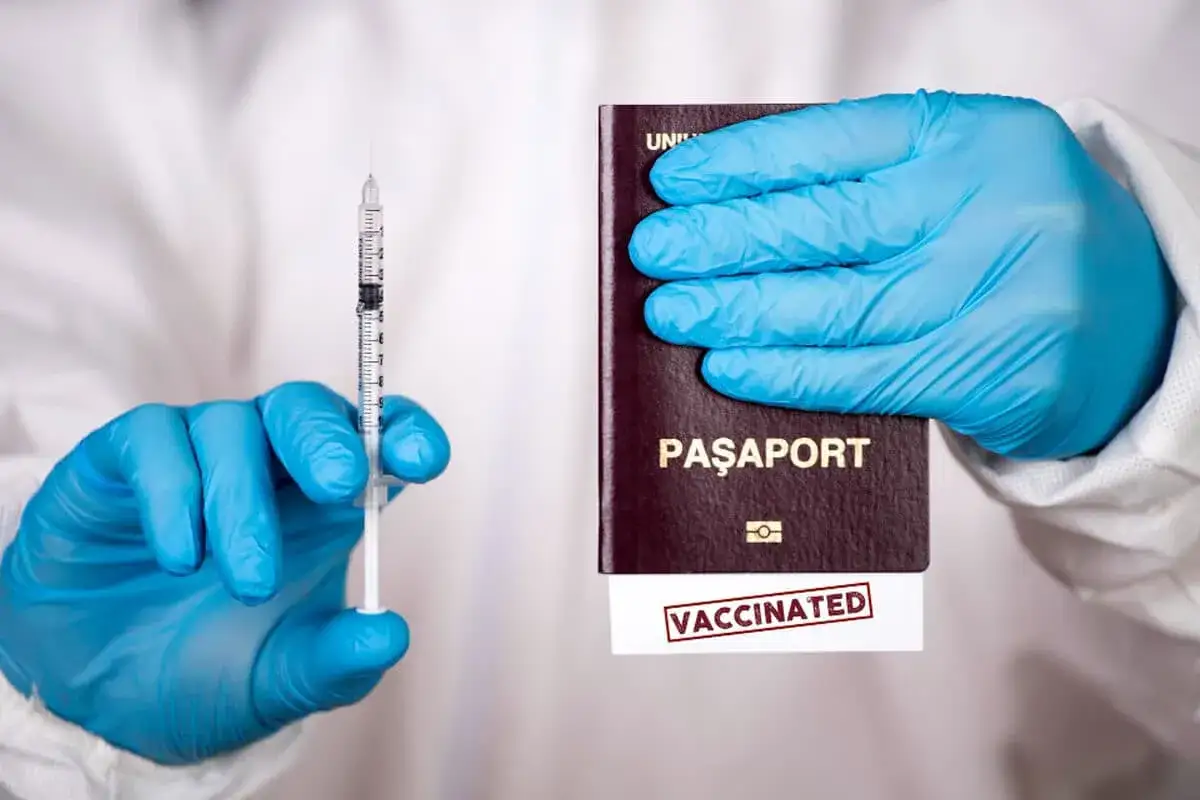 Ręce w niebieskich rękawiczkach trzymają strzykawkę i paszport z pieczątką 