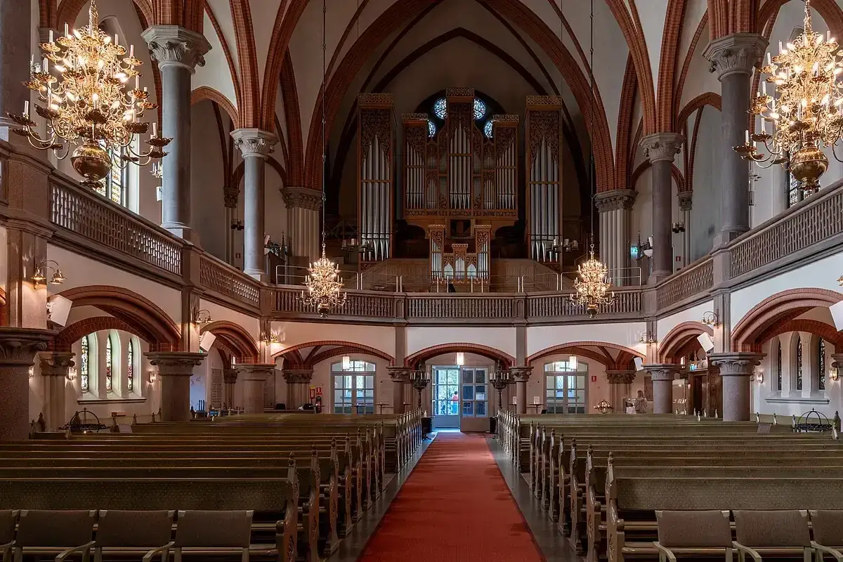 Interiör i Oscars kyrkan med bänkrader, en röd heltäckningsmatta, stora ljuskronor och en imponerande orgel.