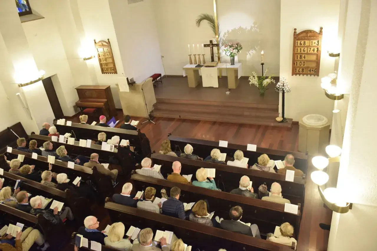 Menschen sitzen in Kirchenbänken, lesen und hören zu. Ein Klavier steht bereit. Warum in der Kirche bleiben? Hier finden sie Gemeinschaft und Ruhe.
