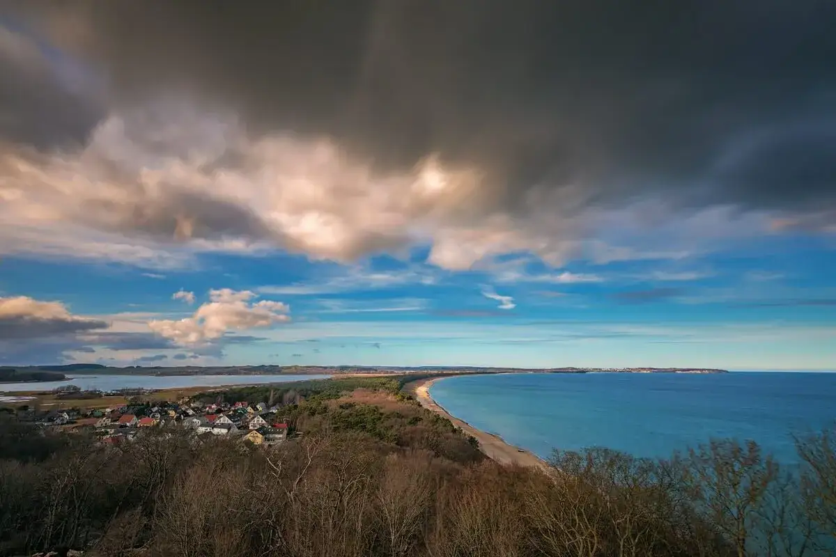 Blick vom Lotsenturm Thiessow über die Küste mit Dorf, Strand und Meer unter dramatischem Wolkenhimmel.