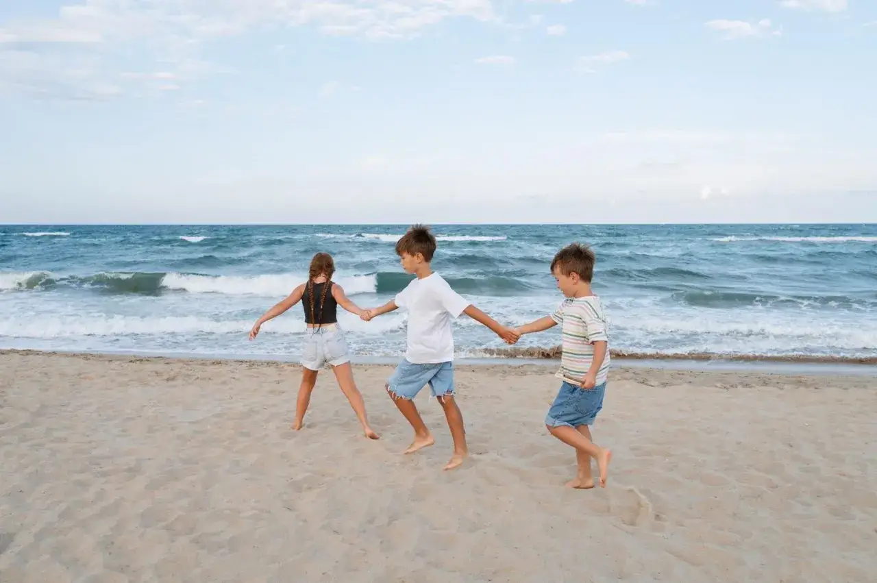Trójka dzieci trzymająca się za ręce na plaży w Pobierowie. Wspaniałe atrakcje dla dzieci nad morzem.