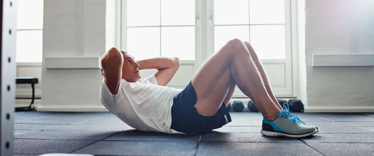 Homme d'&acirc;ge m&ucirc;r faisant des abdos dans une salle de sport, concentr&eacute; sur son entra&icirc;nement.