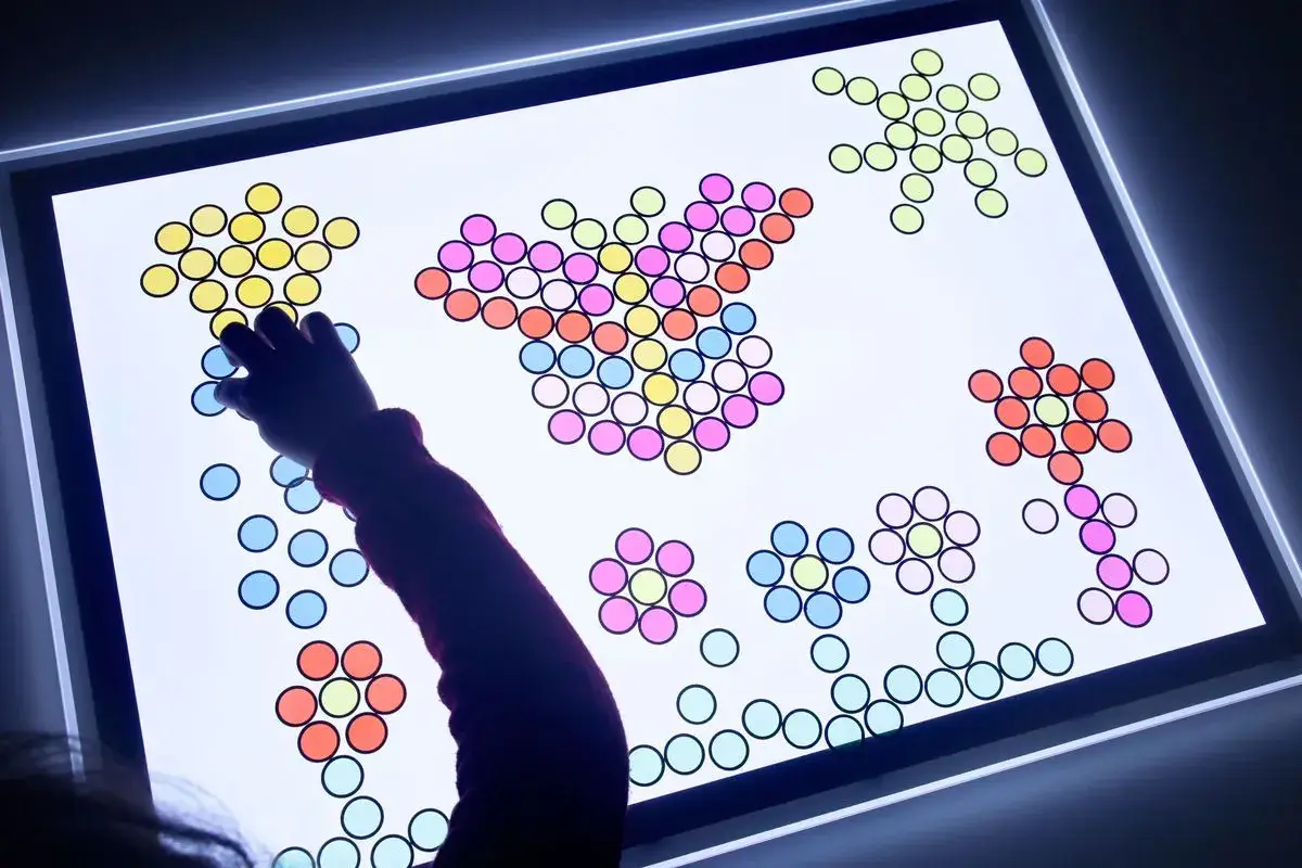Niño/a creando figuras con piezas de colores en una mesa de luz, fomentando sus actividades creativas.