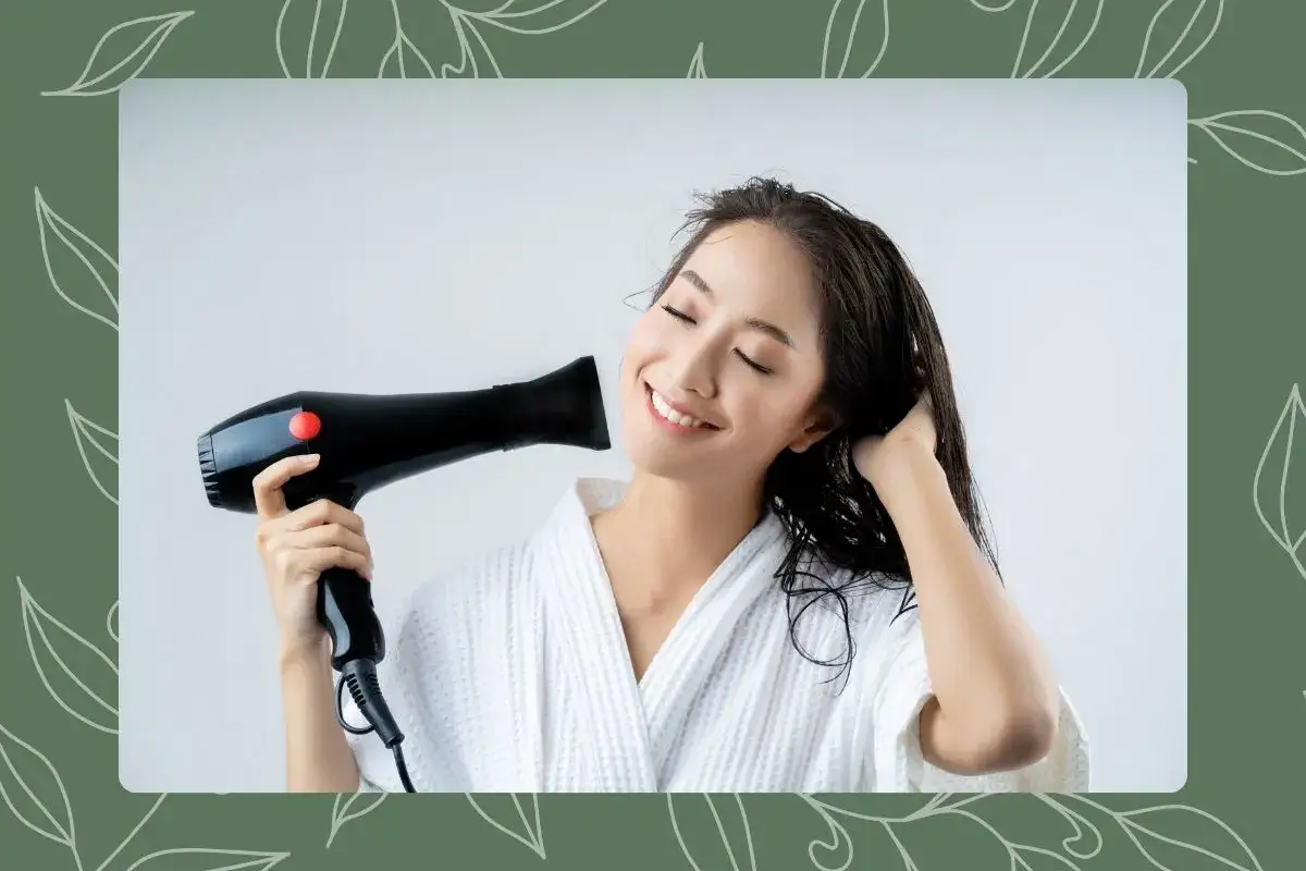 Mujer sonríe mientras se seca el pelo mojado con un secador. Recuerda, es malo dormir con el pelo mojado.