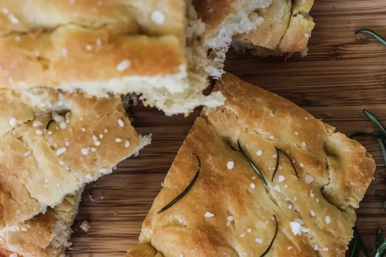 Chleb włoski przepis: puszysta focaccia z rozmarynem i solą morską, pokrojona na desce.