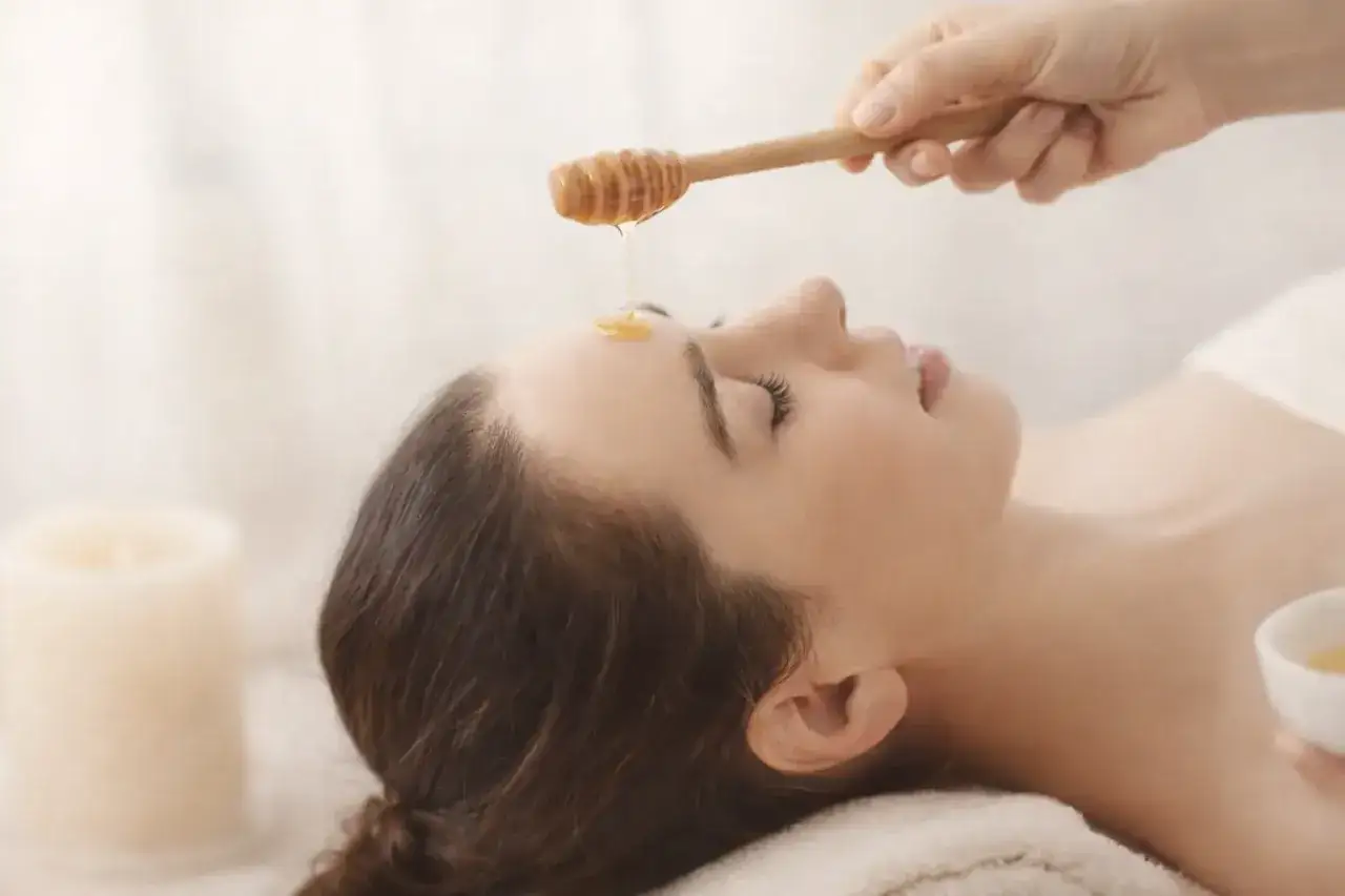 Une main applique du miel sur le front d'une femme allong&eacute;e, profitant des bienfaits du miel sur la peau pour un soin apaisant.