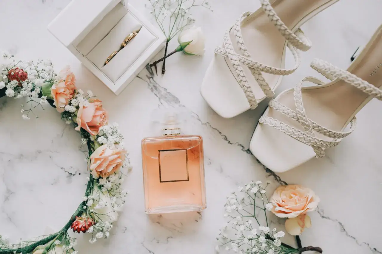 Elegancki flat lay: białe sandałki, pierścionki w pudełku, wianek z róż i gipsówki, perfumy Coco Mademoiselle.