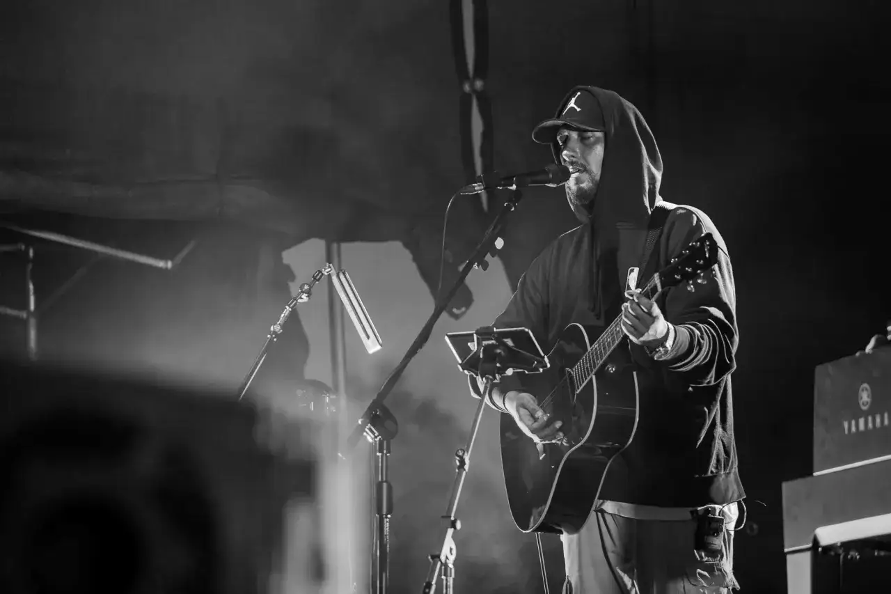 Artysta w kapturze i czapce z daszkiem gra na gitarze, śpiewając do mikrofonu. To jest ten **kortezy co w tobie i we mnie**, muzyka łącząca serca.
