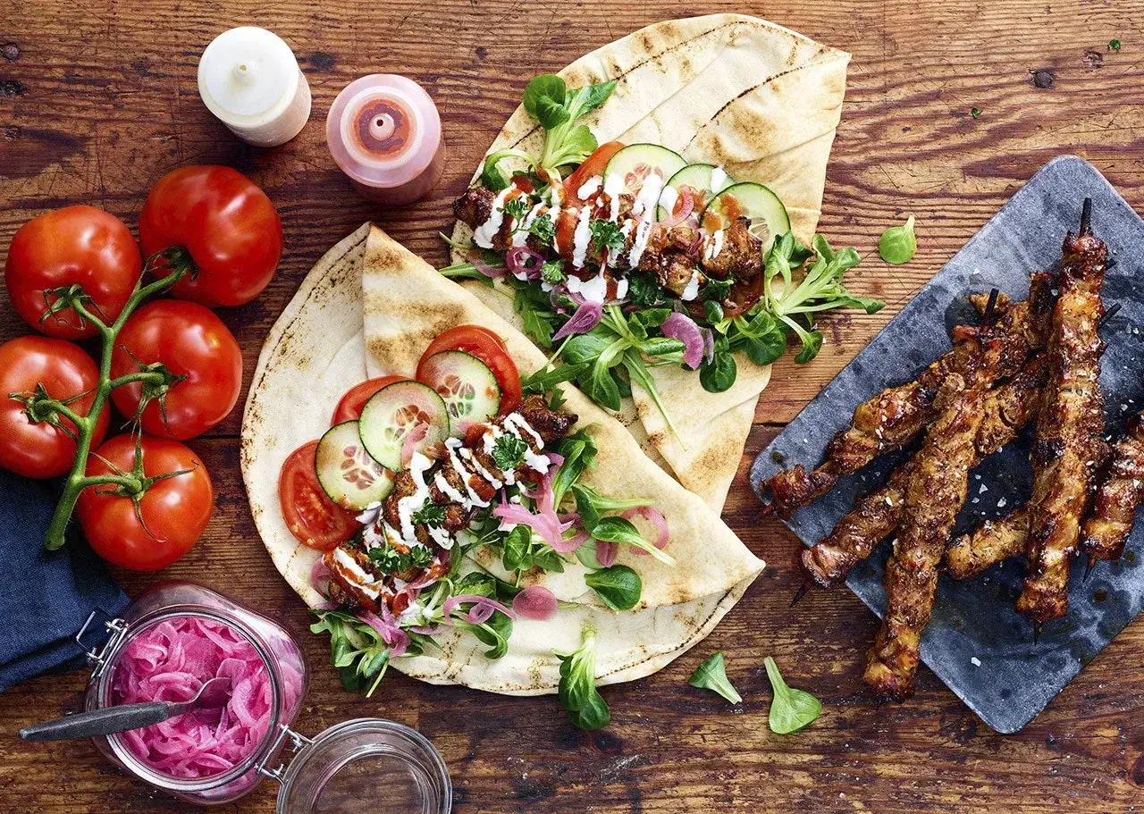 Två wraps med grillad kyckling, grönsaker och sås. Bredvid ligger grillspett med kyckling.