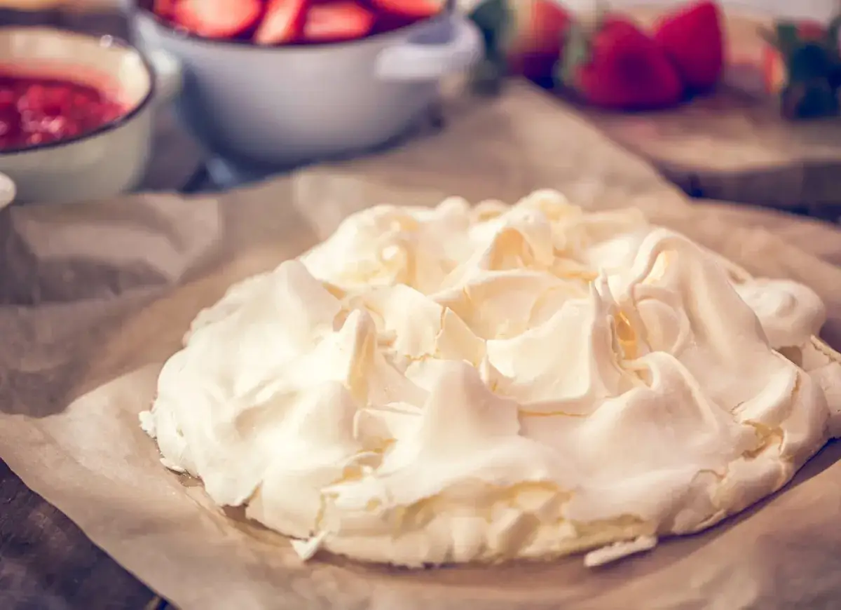 Idealna beza, która nie jest gumowa, powstaje z ubitych białek. Na zdjęciu widać gotowy spód do tortu Pavlova, obok miseczki z truskawkami.