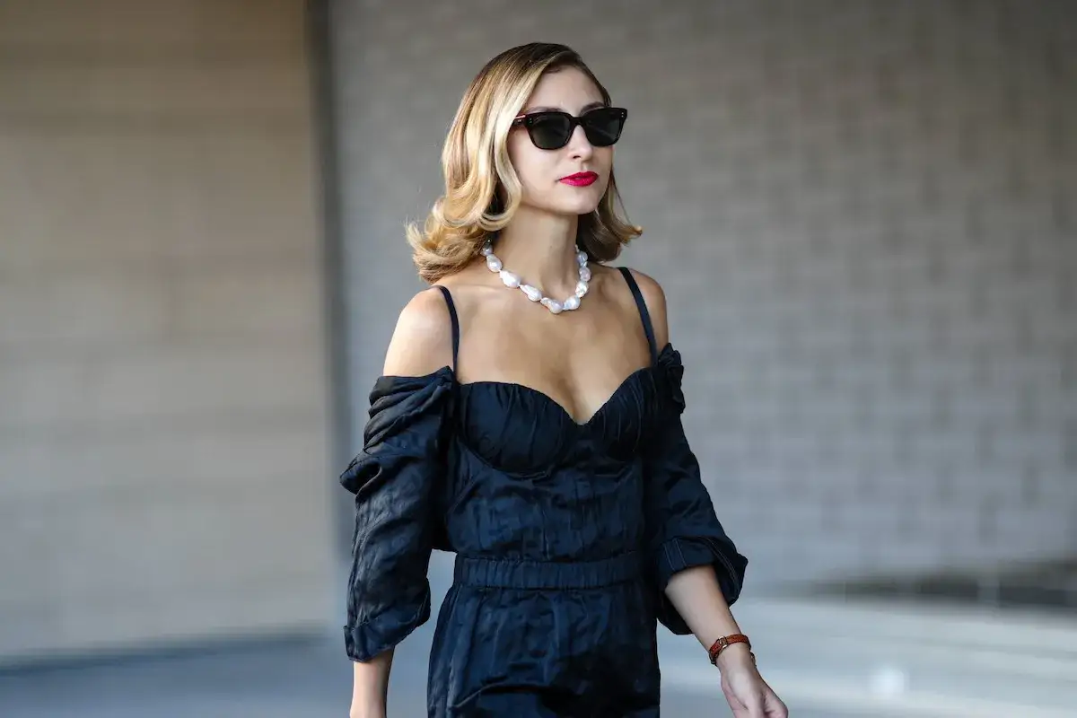 Donna con abito nero elegante, collana di perle e occhiali da sole. Perfetti accessori per abito nero matrimonio.