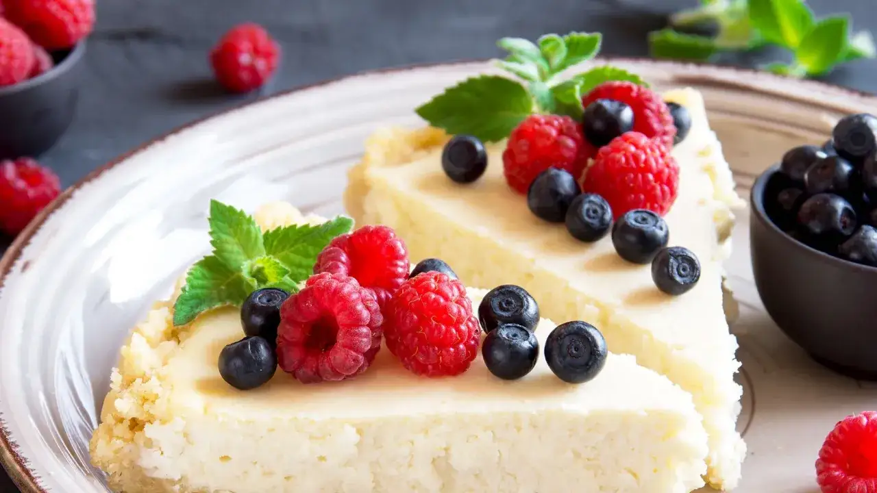 Zwei St&uuml;cke cremiger cheesecake ohne backen, garniert mit frischen Himbeeren, Blaubeeren und Minze.