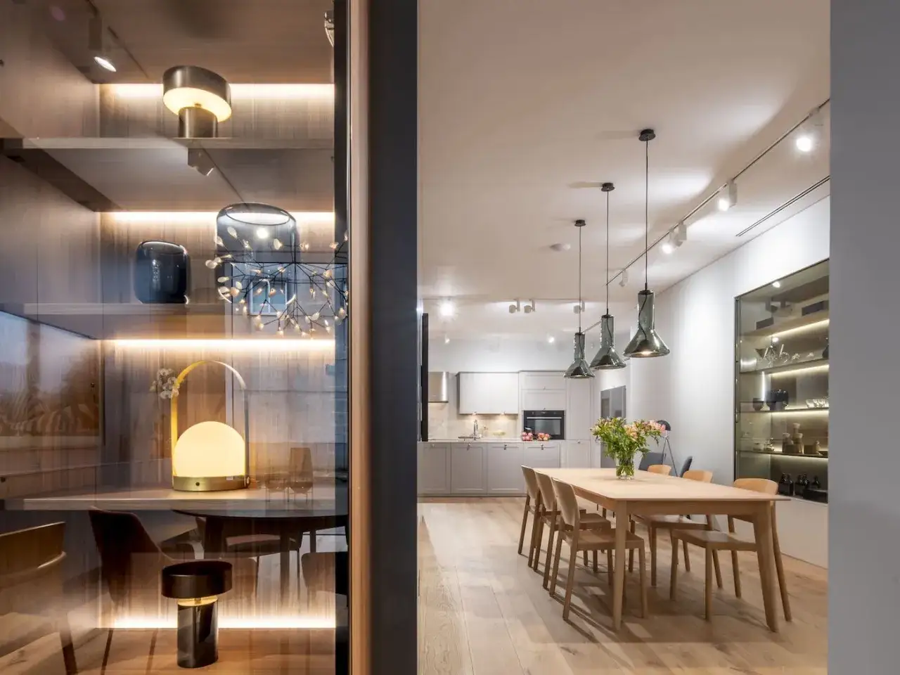 Una barra de focos ilumina la cocina y el comedor. En la estantería, lámparas decorativas y jarrones crean un ambiente acogedor.