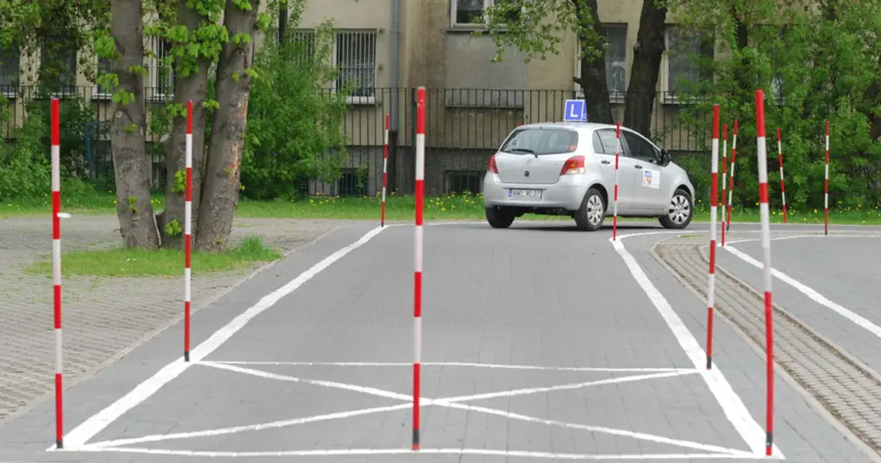 Plac manewrowy z tyczkami i samochodem z literą L. Idealne miejsce na kurs doszkalający dla kierowców kat B.