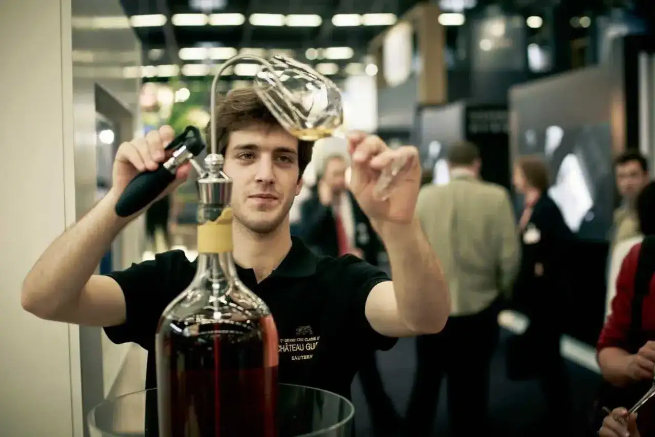 Un homme sert du vin d'une très grande bouteille, peut-être la plus grande bouteille du monde, dans un verre.