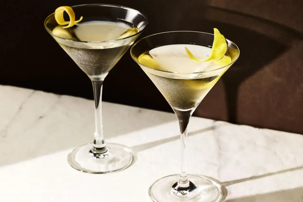 Dwa eleganckie drinki dry martini, każdy ozdobiony skórką cytryny. Idealne na wieczór, gdy szukasz inspiracji na drinki.
