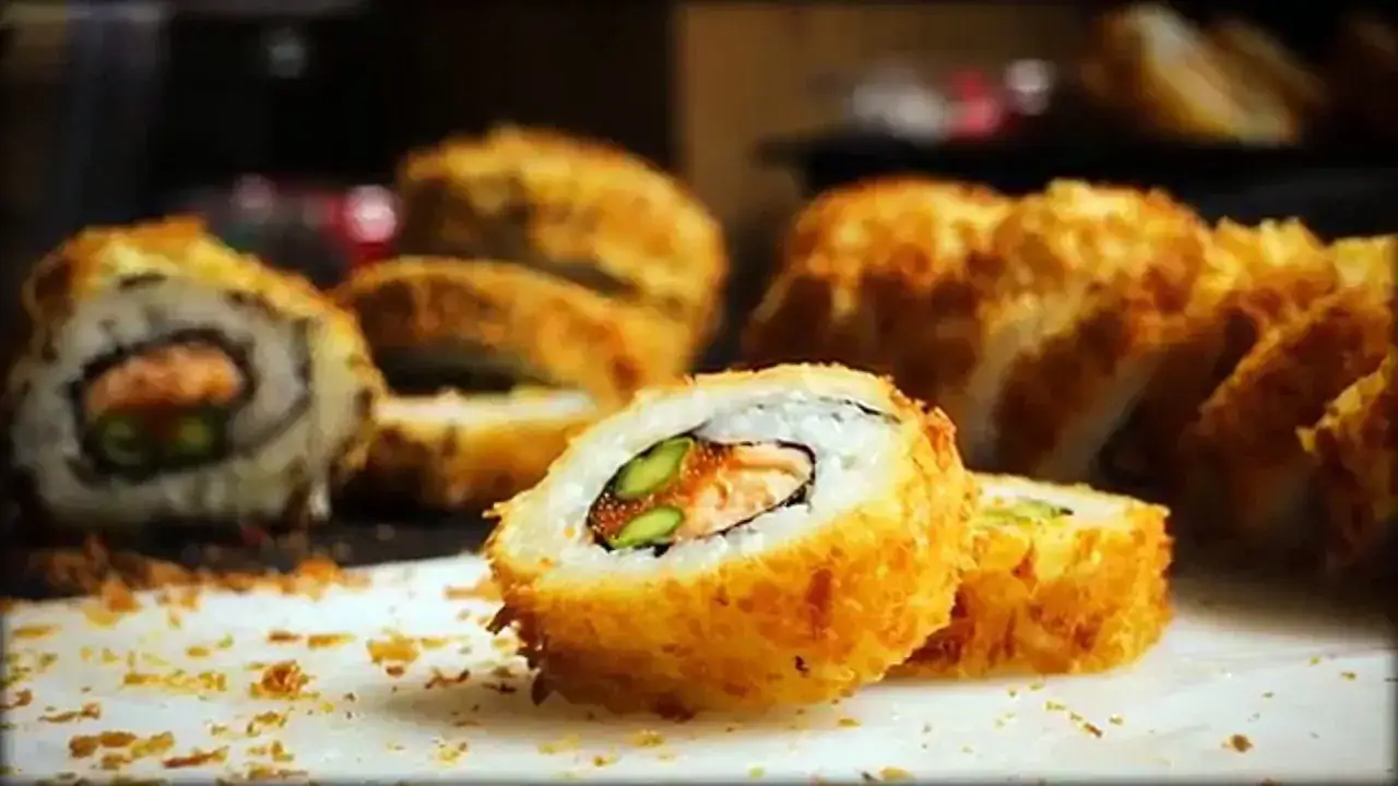 Knusprig frittiertes Sushi mit Lachs und Spargel, auf einem weißen Teller mit Krümeln.