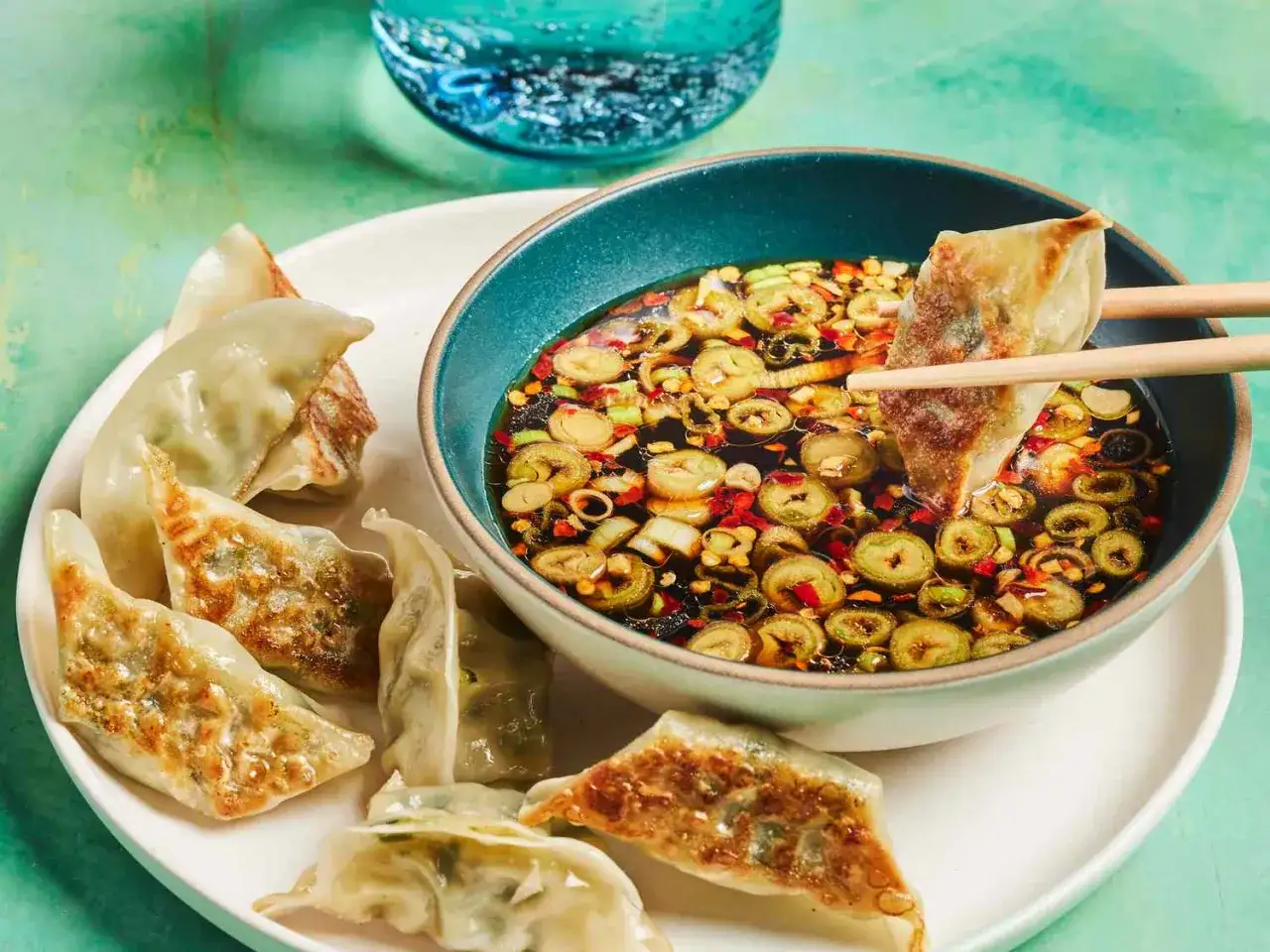 A gyoza is dipped into a flavorful gyoza dipping sauce with scallions and chili flakes.