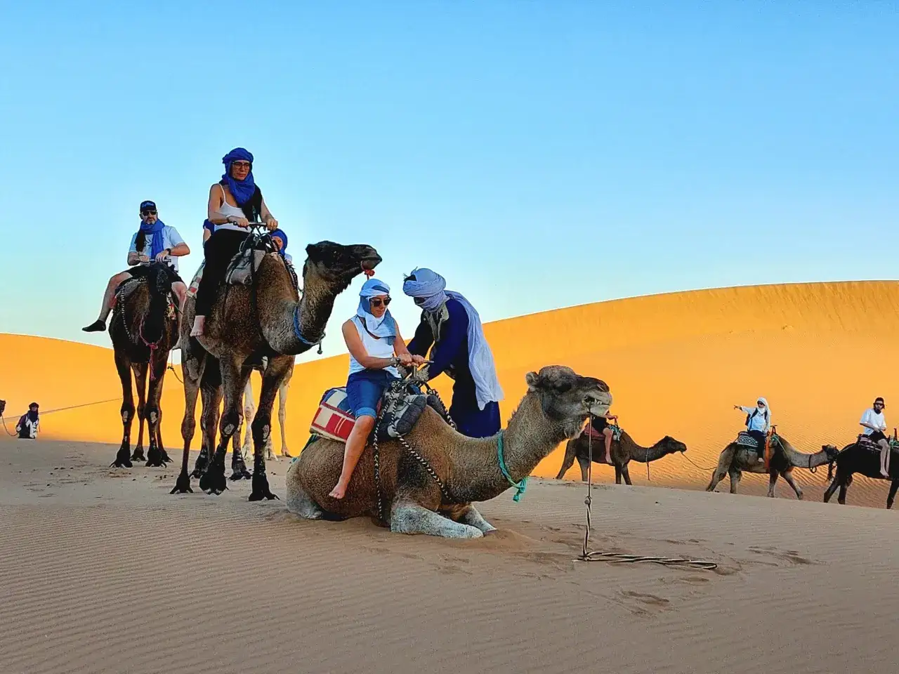 Viaje de marruecos 5 días: personas montan camellos en el desierto al atardecer.