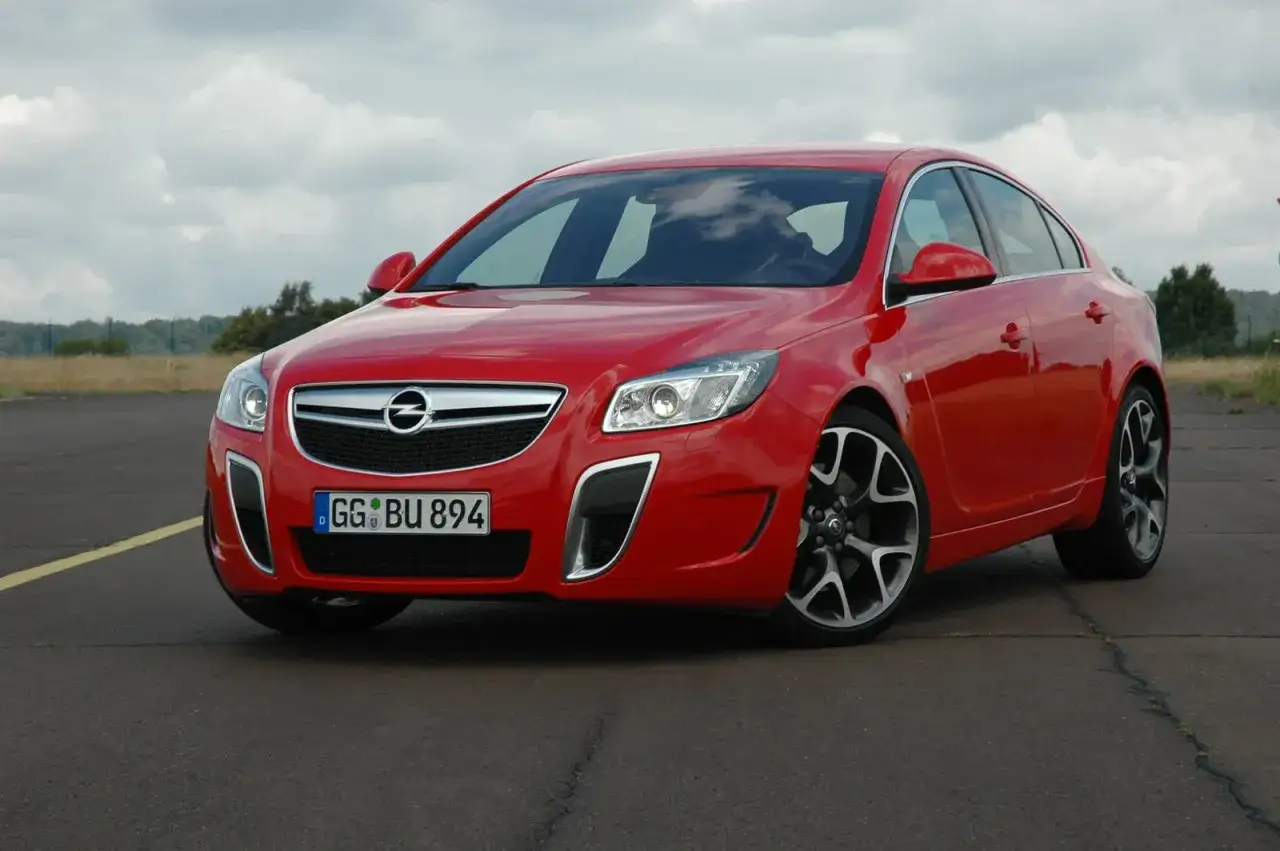 Czerwony Opel Insignia z nowoczesnymi żarówkami z przodu, zaparkowany na pustej drodze.