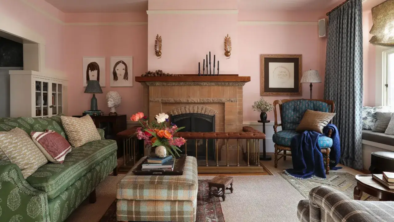 Gemütliches Wohnzimmer mit rosa Wänden. Ein grünes Sofa, karierter Hocker und ein Kamin. Welche Farbe passt zu rosa? Grün und Blau harmonieren wunderbar.