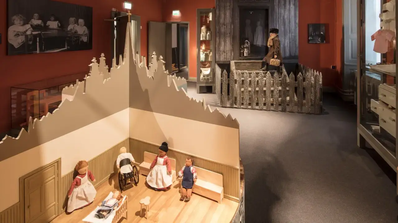 En utställning på stadsmuseet i Stockholm visar dockor i en barnkammare och en historisk scen med en kvinna.