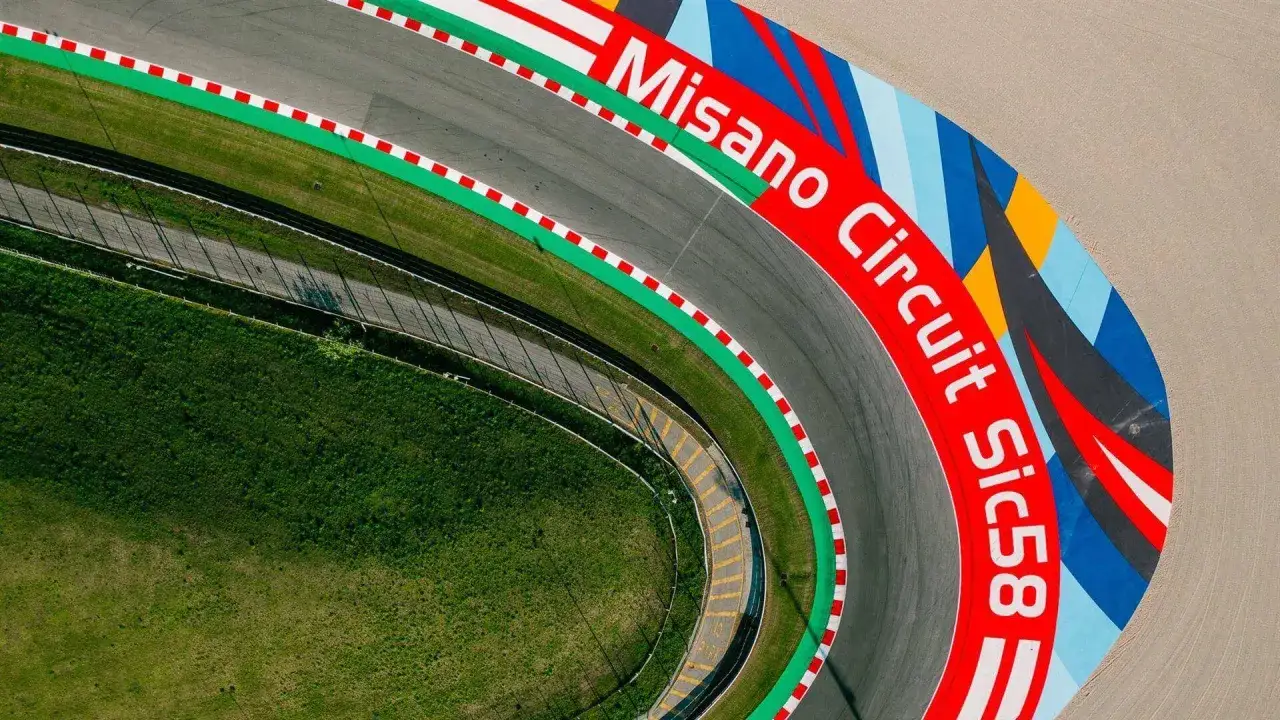 Vista aerea del Misano Circuit Sic58, con la pista grigia, erba verde e colorate decorazioni sul bordo.