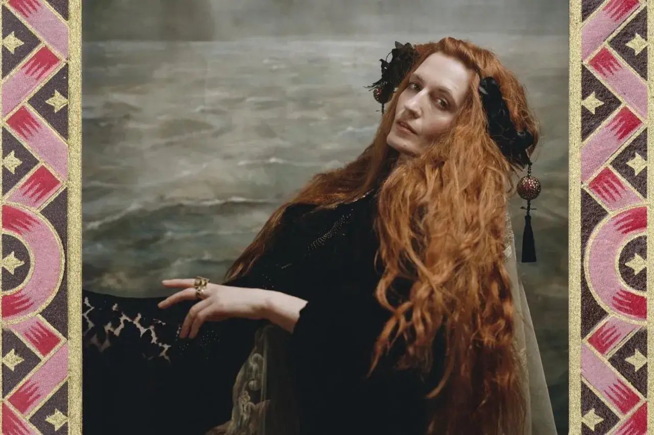 Florence Welch, jak królowa, z rudymi włosami i ozdobami we włosach, na tle morskiego pejzażu.