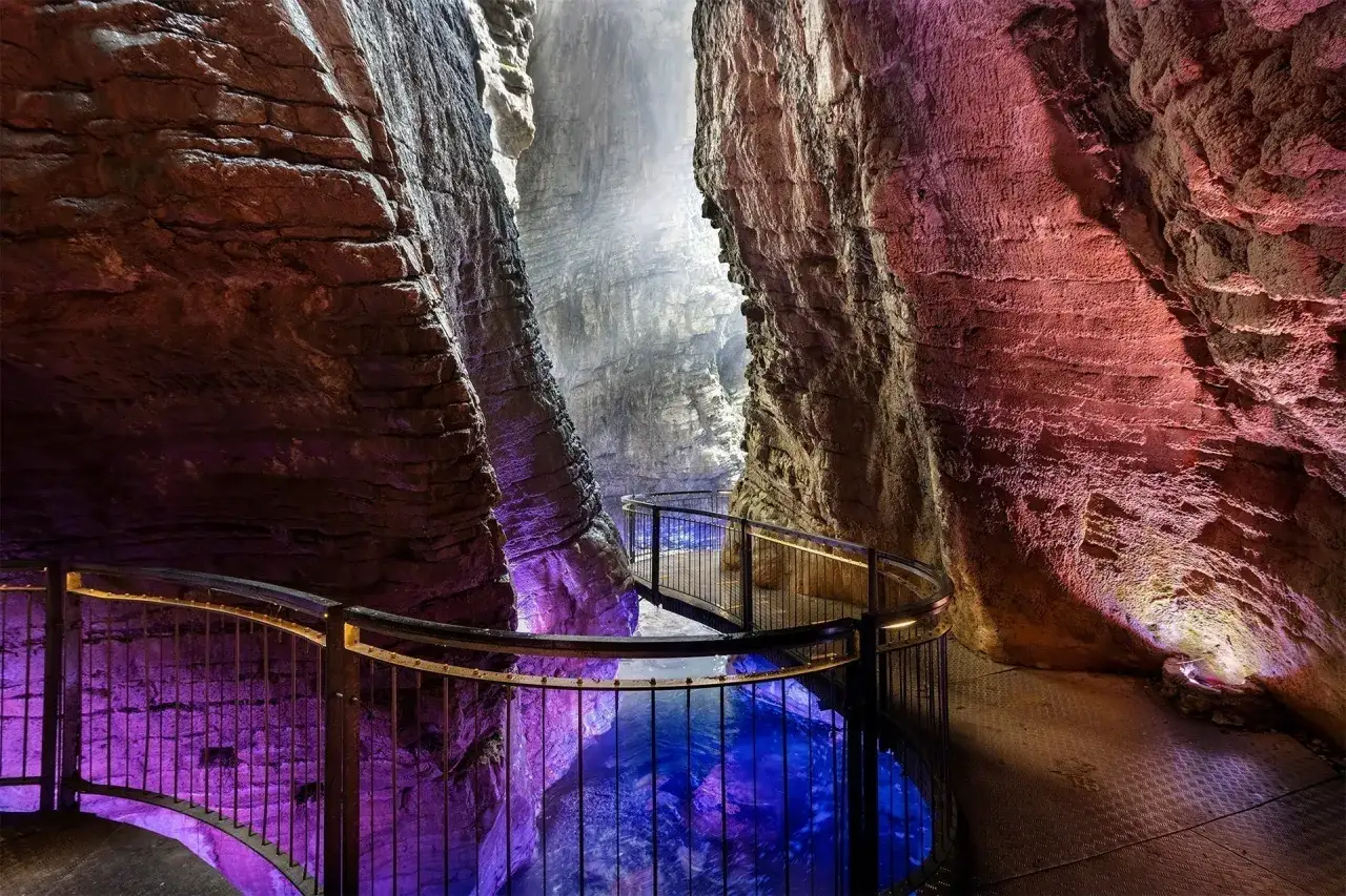Sentiero illuminato tra rocce scolpite, con acqua blu intenso e luci viola che ricordano le cascate del Lago di Garda.