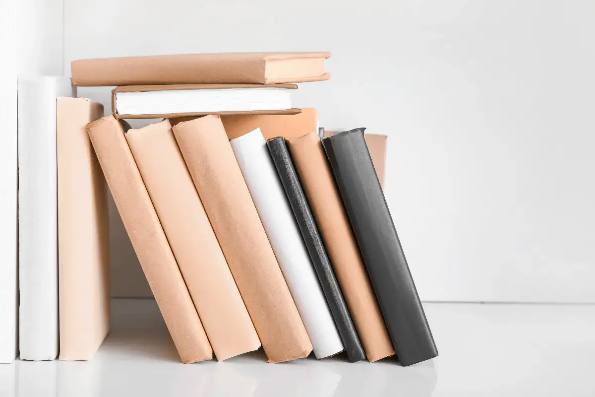 Kalkulacja kosztów samodzielnego wydania książki (self-pub). Stos książek w różnych okładkach, od białych po brązowe i czarne.