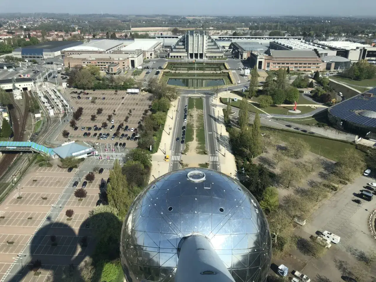 Vista aérea del Atomium, un lugar icónico para viajar a Bruselas. Se aprecian edificios, estacionamientos y un estanque.