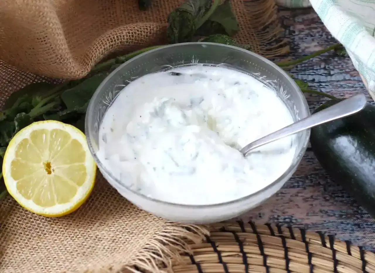 Un cuenco de cremosa salsa de yogur con hierbas, acompa&ntilde;ado de un lim&oacute;n fresco y un calabac&iacute;n.
