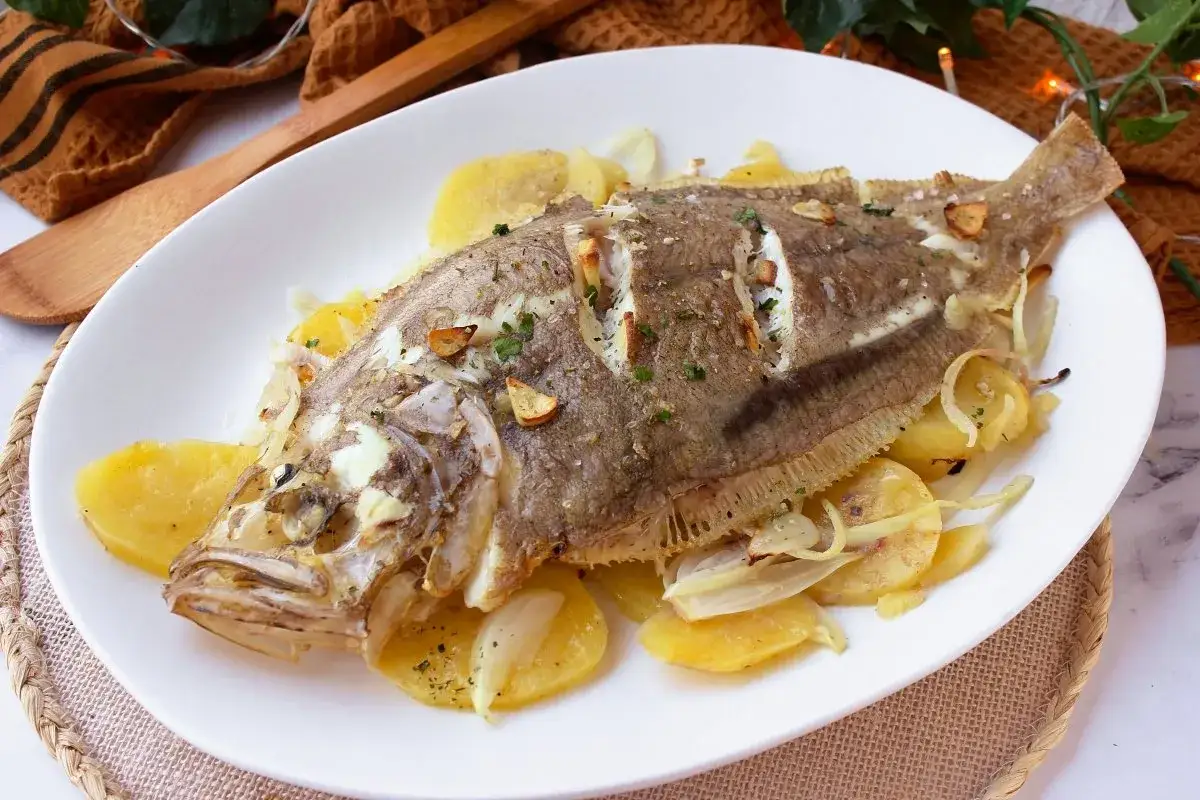 Delicioso gallo al horno con patatas y cebolla, servido en plato blanco.