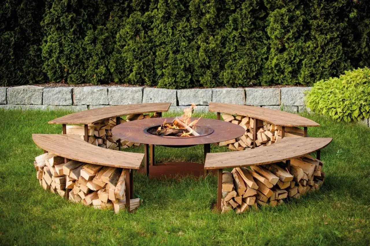 Gemütliche Grillecke im Garten mit Feuerstelle und Sitzbänken aus Holz, die gleichzeitig als Holzstapel dienen. Tolle Gartenideen für gesellige Abende.