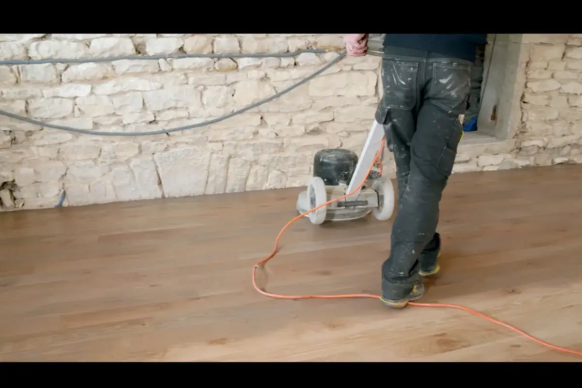 Un ouvrier applique de l'huile sur un parquet en bois avec une ponceuse.