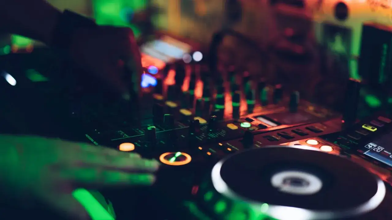 DJ-H&auml;nde bedienen einen Mixer, um einen perfekten Mixtape zu erstellen. Gr&uuml;ne und rote Lichter beleuchten die Szene.