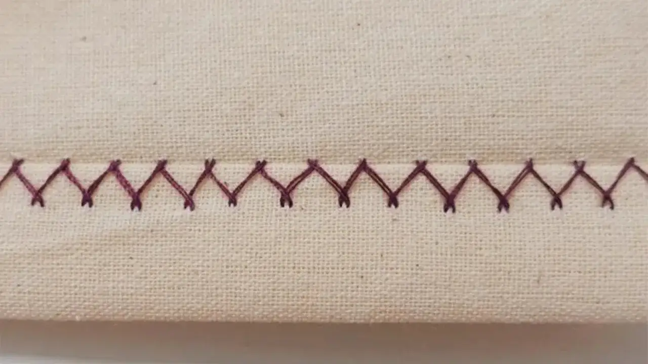 A zigzag stitch on a beige fabric. This stitch is often used to finish the raw edge of fabric, preventing fraying.