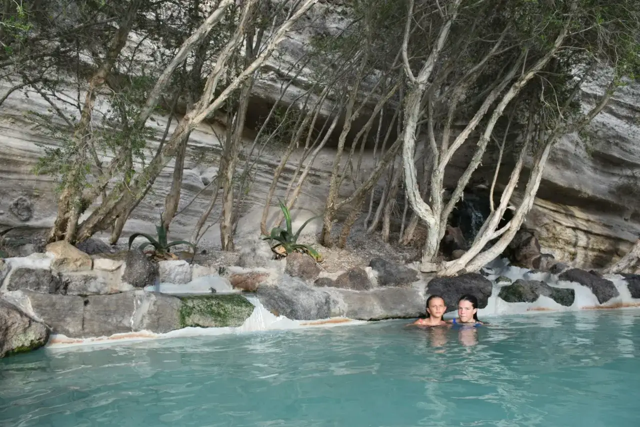 Due bambine si godono l'acqua calda di una spiaggia naturale a Ischia, circondate da rocce e vegetazione.